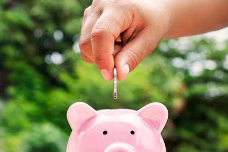 Close-up shot of a woman putting a coin in a piggy bank. Money saving concept.の写真素材