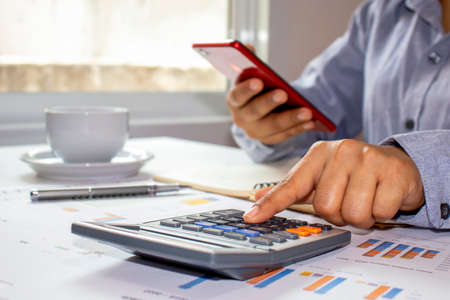 Women use calculators to calculate annual reports, including notebooks on wooden desks for work, work concepts, and account management.の写真素材