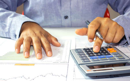 Close-up of a woman examining an accounting report and using a calculator for financial auditing...