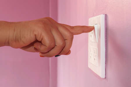 The finger is pressing the switch to turn off household electrical appliances to save energy.