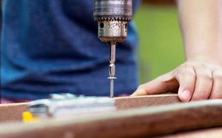 The carpenter uses a drill to tighten the screws to the plank.