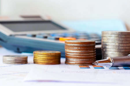Pens, coins, and calculators placed on financial reports or stock market graph analysis.の写真素材