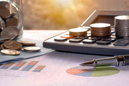 Pens and coins placed on financial reports or stock market graph analysis.の写真素材
