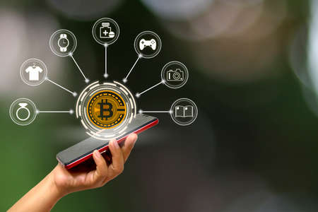 Close-up of a woman's hand holding a smartphone with a hologram, bitcoin symbol and an online...