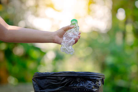 Young woman holding garbage or plastic bottle thrown into the trash on natural green background....