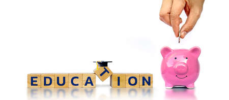 Education letter on square wooden cube and holding money into piggy bank to save money separately on white background.の写真素材