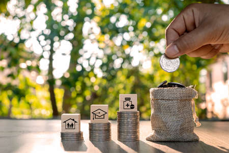 The hand is holding a coin in a money-saving bag and family, education and health icons on the stack...