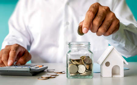 Businessman putting money in a savings bottle and house model, financial concept. Home Mortgage and...