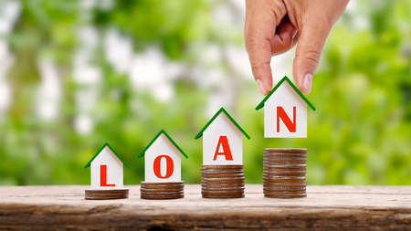 Hand holding a house model with loan text and a small house model on a pile of real estate...