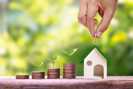 Hand holding coins put in house model for saving money and trees growing on a pile of money finance concept. Business and real estate investmentの写真素材