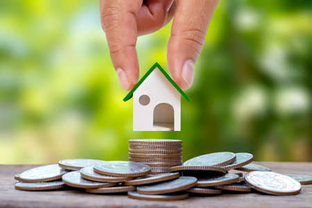 Hand-holding model house on a pile of coinsの写真素材