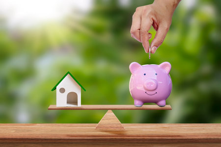 Model house and hand holding a coin in a pig piggy bank placed on the scales and blurred green background. Real estate ideas and future investment business plans.の写真素材