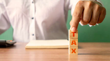 Young woman holding a wooden cube with the word Tax, financial concept. Financial Management and Tax Planningの写真素材