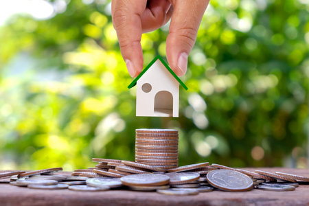 Hand holding mock house on a pile of coins with blurred green nature background, home loan and real estate investment loan.の写真素材
