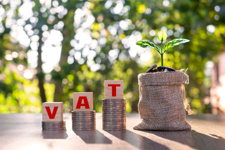 Wooden block with vat text on stacked coins and tree on tong vat concept VAT charged by the government on the purchase of goods or services.の写真素材