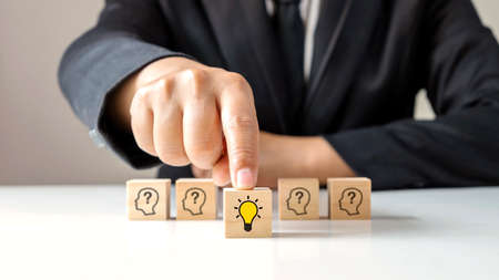 Businessman choosing light bulb icon, full of ideas and creativity on the wooden cube, financial planning ideas to achieve goals.の写真素材