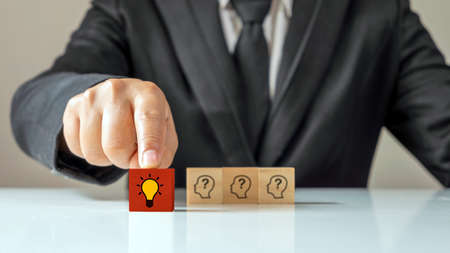 Businessman choosing light bulb icon, full of ideas and creativity on the wooden cube, financial planning ideas to achieve goals.の写真素材