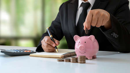 Close-up of a businesswoman holding a coin in a piggy bank, a concept of saving money for financial accounting.の写真素材
