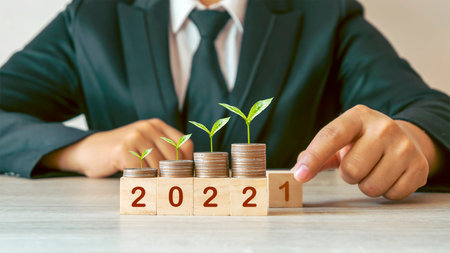 happy new year 2022 hand is changing wooden cube from number 2021 to 2022 and tree growing on pile of coinsの写真素材