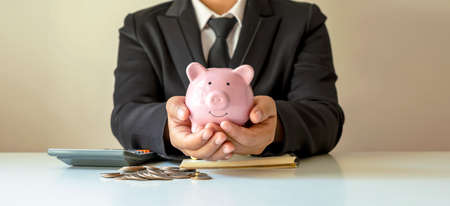Businessman holding piggy bank for saving money, the money-saving concept for investment.の写真素材