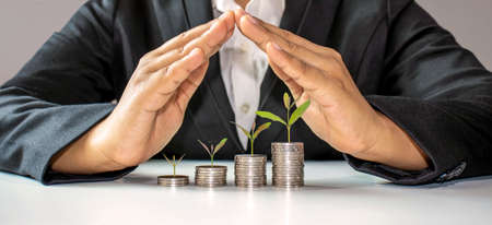 trees growing on a pile of coins in the hand of a middle-aged man. Retirement Financial Planning Ideas saving money and cash and investment to create financial stability after retirementの写真素材