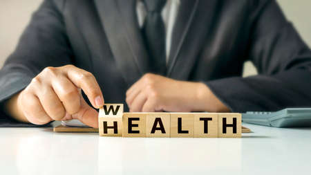A businessman selects a goal printed on a wooden cube block with the message Wealth and Health. financial wealth concept Investing in life and health insuranceの写真素材