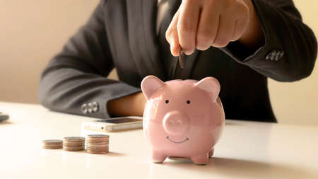 Businesswomen who hold coins in a piggy bank closely, including pressing a calculator for...