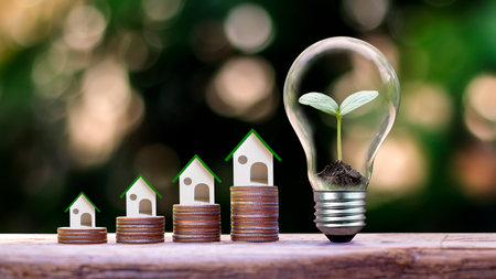 Model wooden house on a stack of coins and planted in a light bulb.の写真素材