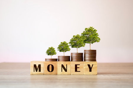 The text MONEY on a wooden cube and a tree growing on a pile of coins. Financial concepts for business management.の写真素材
