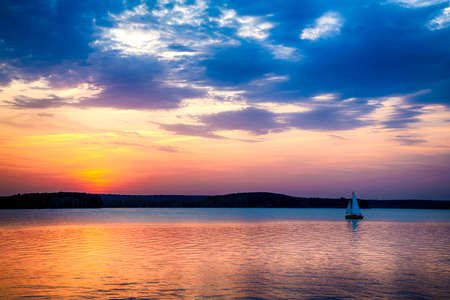 Sailboat sunset fantasy sailing along its journey against a vivid colorful sunset in formation against an orange and yellow color filled sky.の写真素材