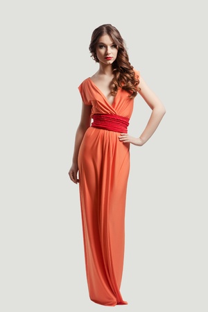 Model with beautiful long hair posing in orange dress isolatedの写真素材