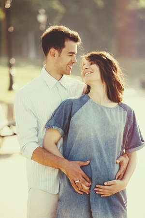 Happy and young pregnant couple hugging in nature. Vintage retro style with light leaksの写真素材