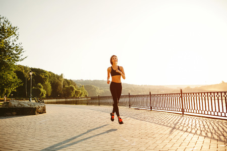 Running woman. Runner jogging in sunny bright light. Female fitness model training outside in park