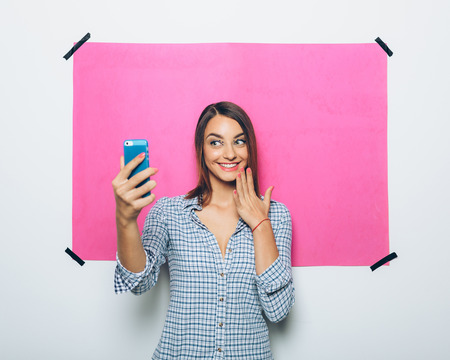 Pretty young woman taking picture with camera phone over pink backgroundの写真素材
