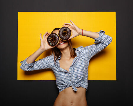 Girl holding a donut with chocolate icing on yellow backgroundの写真素材