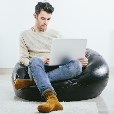 Fashionable man in winter knitted clothes sits with laptop on his kneesの写真素材