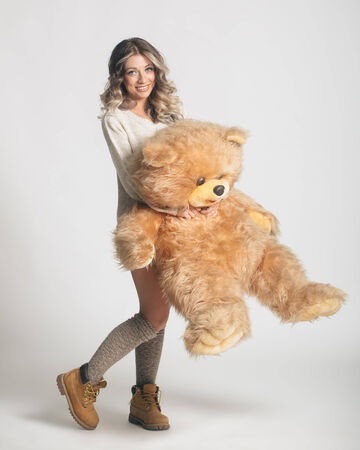 Casual smiling young woman in winter clothing holding big soft teddy bear on white backgroundの写真素材