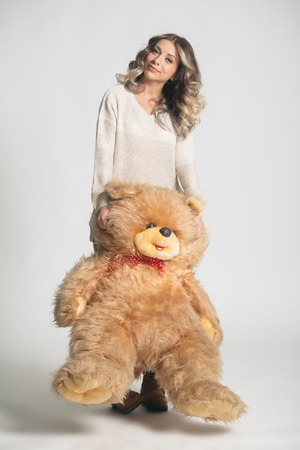 Casual smiling young woman in winter clothing holding big soft teddy bear on white backgroundの写真素材