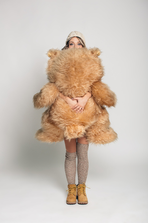 Casual smiling young woman in winter clothing holding big soft teddy bear on white backgroundの写真素材