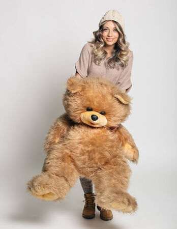 Casual smiling young woman in winter clothing holding big soft teddy bear on white backgroundの写真素材
