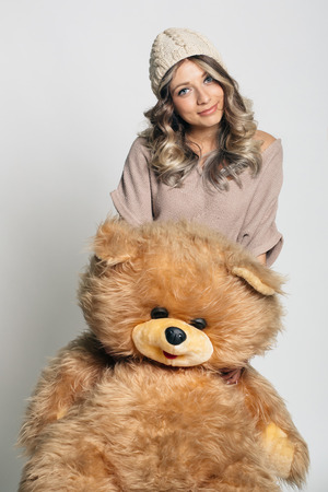 Casual smiling young woman in winter clothing holding big soft teddy bear on white backgroundの写真素材