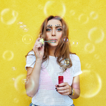 Young woman portrait blowing soap bubbles over yellow backgroundの写真素材