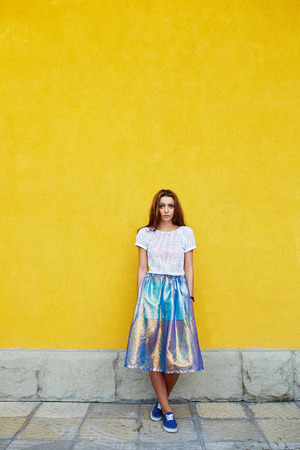 Attractive girl in an unusual skirt posing near a yellow wallの写真素材