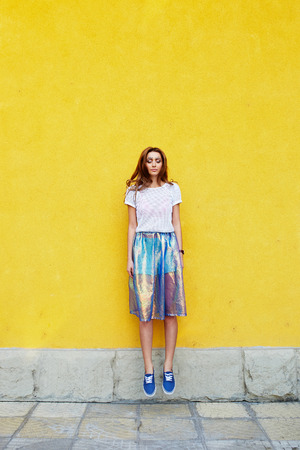 Attractive girl in an unusual skirt posing near a yellow wallの写真素材