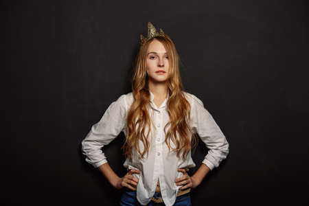 Attractive girl portrait in a white shirt with a crown on her head on a black backgroundの写真素材