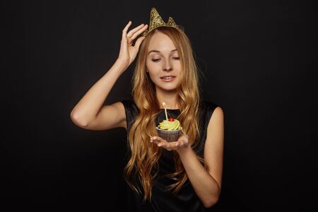 Attractive girl with a crown on her head in a white black is holding cupcakeの写真素材