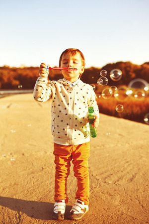 Little boy playing with soap bubbles. Warm filter and film effectの写真素材
