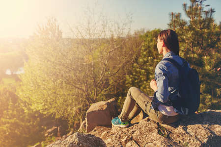 Young woman with backpack sitting on cliff in the parkの写真素材