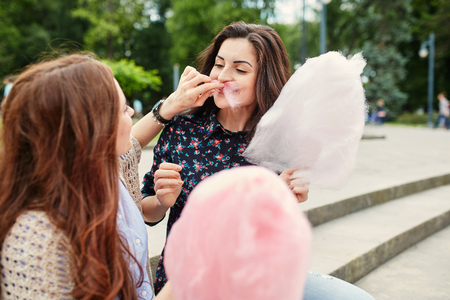 Two cheerful sisters eating cotton candy at the parkの写真素材