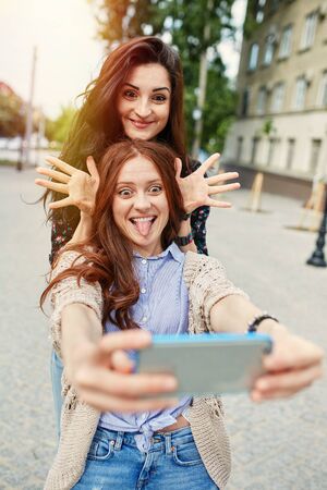 Sisters making selfie. Two beautiful young woman making selfie and grimacing on the mobile phone. Light leak effectの写真素材